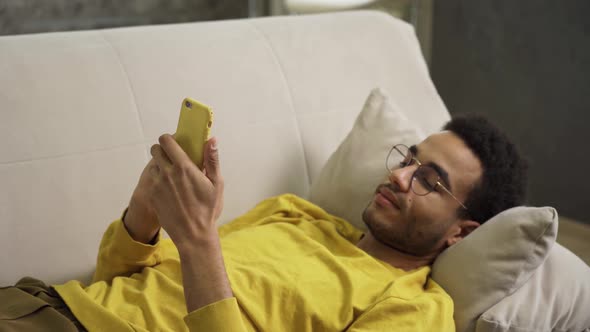 Young African Lying on the Couch Using a Smartphone