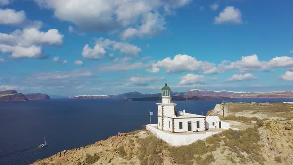 4k aerial drone orbit flying around beautiful lighthouse Santorini Greece with blue sky and clouds