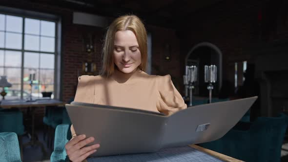 Portrait of Confident Caucasian Woman Sitting in Sunshine in Restaurant Examining Menu and Looking