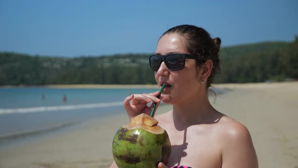 Young Woman in Sunglasses Drinks Coconut on the Beach