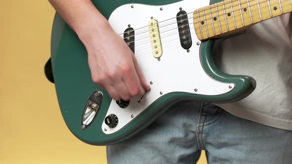 Cropped Photo of Young Male Musician in Jeans Tuning Electric Guitar Before Playing Isolated Over