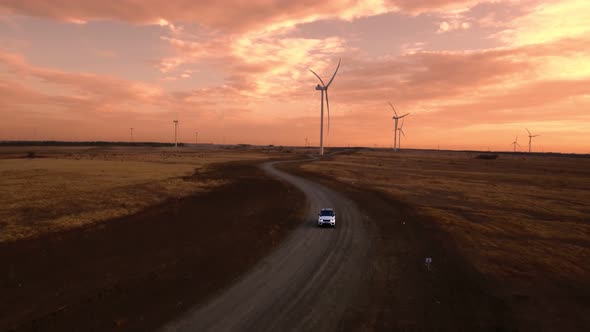 Aerial View Car Drives in Field Against Backdrop Windmill and Beautiful Sunset