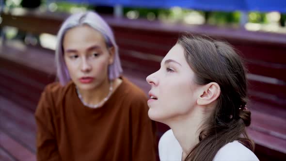 Modern Teenage Girls with Colorful Dyed Hair Sitting on Bench in Park. Women Chatting, Gossiping