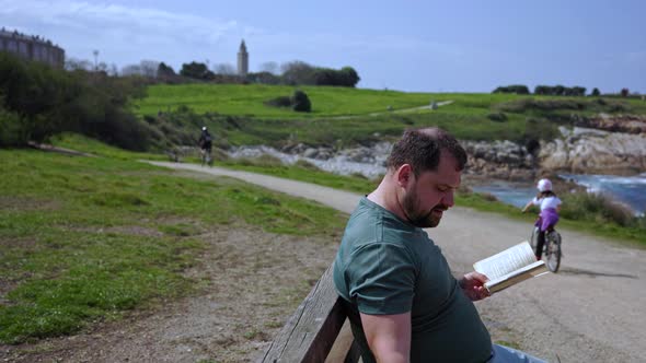 A Man Sits on a Park Bench Reading a Book