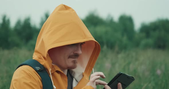 Man is Raincoat with Hood is Talking on Phone in Nature Connection Interrupted