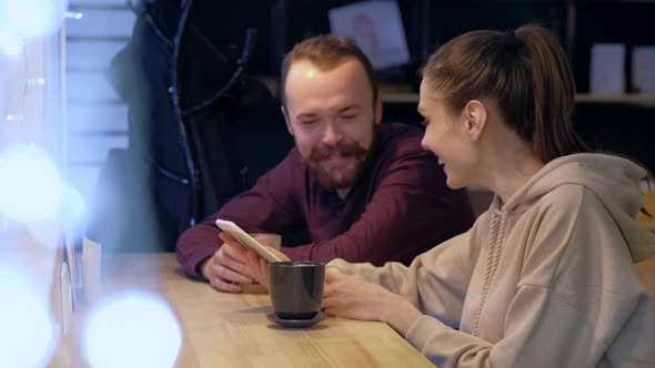 A couple sitting in a cafe, talking, drinks coffee and watching in smartphone.