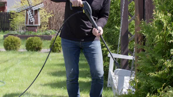 Caucasian Man Disinfects a Bench Hanging on Chains with a High Pressure Washer