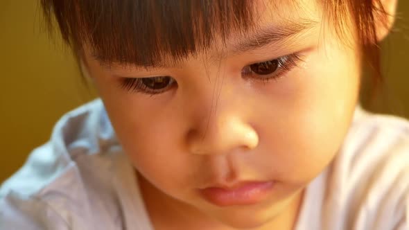 A little cute girl reading a book sits on table at home.