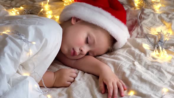 Cute Sleeping Boy in Santa Claus Hat Lying in Bed at Home