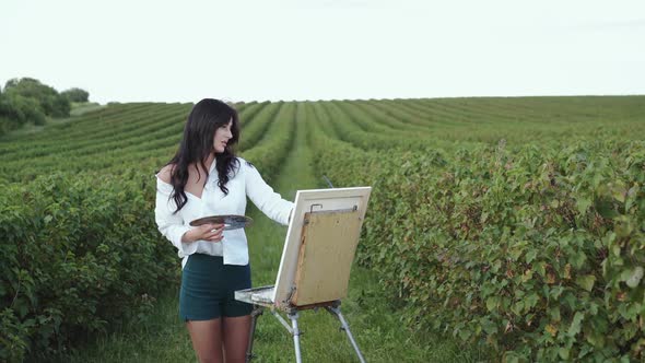 Portrait of Beautiful Girl Rejoices From Painting in a Windy Field