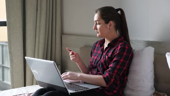 Young Woman in Red Shirt Looks at Credit Card and Types