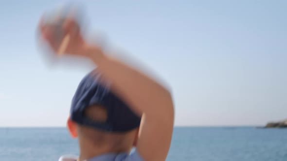 Boy and dad throws a pebble at sea. Family  sitting with back forward at beach on sunny summer day.