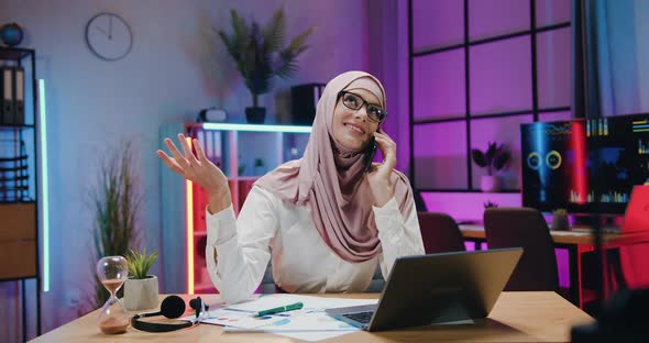 Businesswoman in Light Violet Hijab Enjoying Phone Conversation in Evening Office