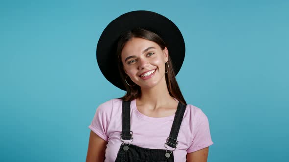 Young Smiling Woman in Hat Looking To Camera. Portrait of Cute Beautiful Hipster Girl on Blue Studio