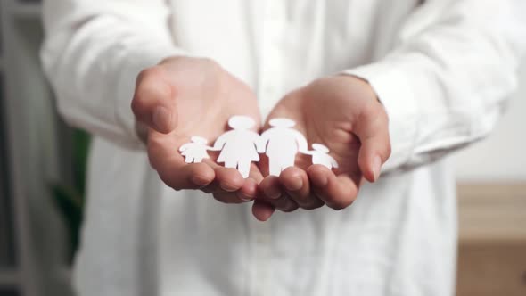 Close Up Female Hands Hold A Young Family Cut Out Of A Paper Sheet, A Symbol Of Well Being