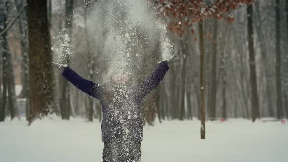 Child Plays in the Winter in the Park Tosses Snow Up. Throws Snowflakes and Smiles in a Winter Park