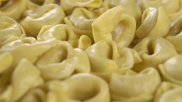 Raw dry tortellini pasta in a white bowl. Falling in slow motion