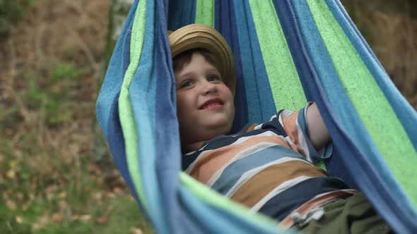 Happy kid boy in hammock in summer garden