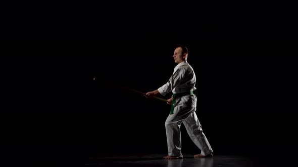 Kendo Fighter on White Kimono Practicing Martial Art with the Bamboo Bokken on Black Background.