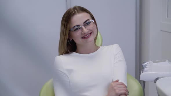 Female Patient with Glasses Sitting on Dental Chair and Smiling at Camera