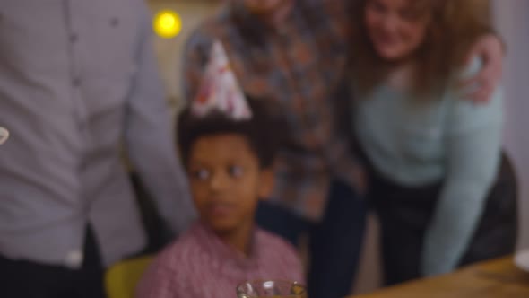 Happy African Preteen Boy Blowing Out Candles on Birthday Cake Celebrating with Family