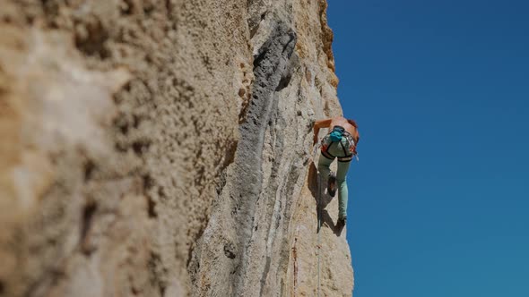 Side View of Young Strong Man Rock Climber in Bright Blue Pants Climbing on Cliff