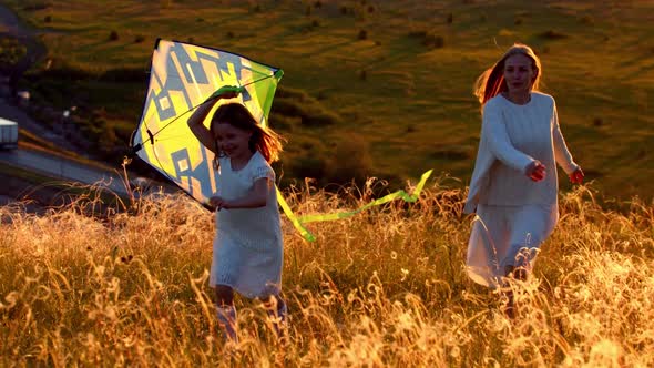 Young Mother with Her Daughter Running on the Hill with the Kite at Sunset