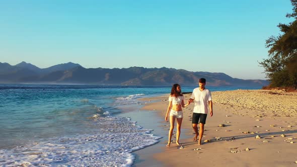 Man and woman sunbathing on tropical coastline beach holiday by blue water with white sandy backgrou