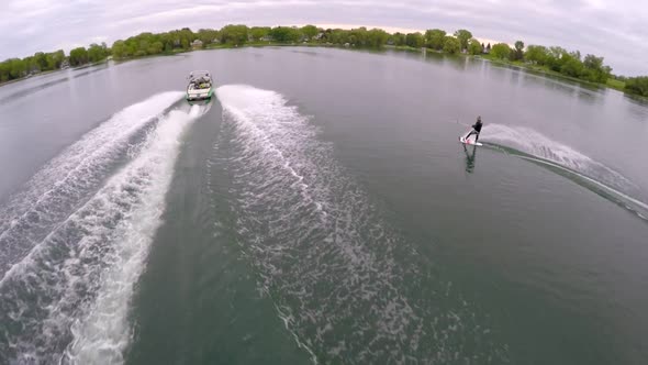 Aerial birds-eye drone view of a man wakeboarding behind a boat.