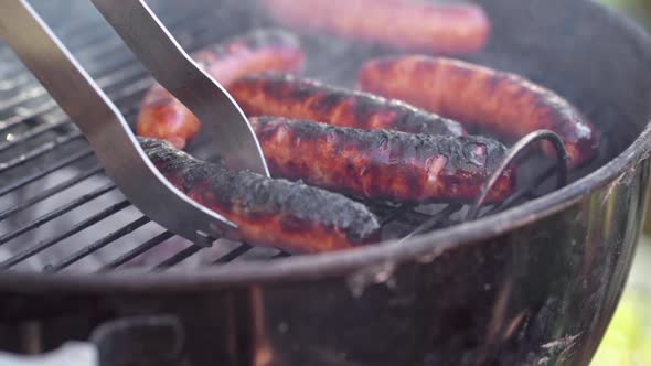 Slow Motion of Tongs Picking Up a Gristly Sausage From Smokey BBQ Grill