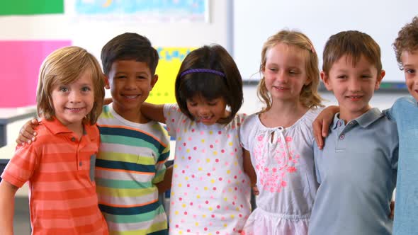 Smiling kids standing with arm around in classroom