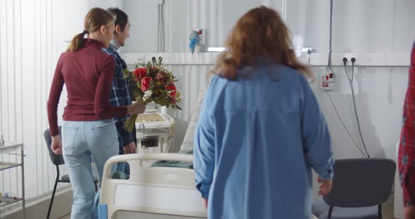 Group of Friends Visiting Sick Young Man in Hospital and Bringing Flowers