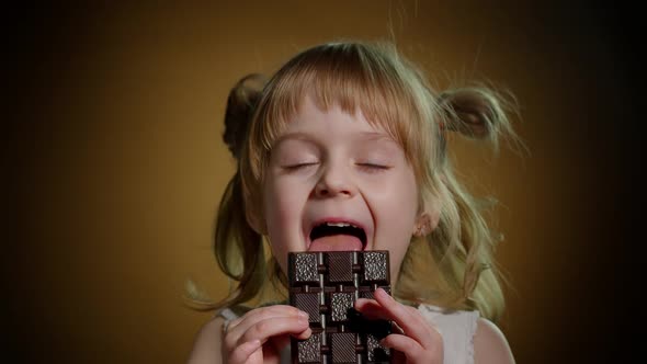 Little Child Girl Kid Eating Chocolate Bar Dessert Showing Thumbs Up Isolated on Dark Background