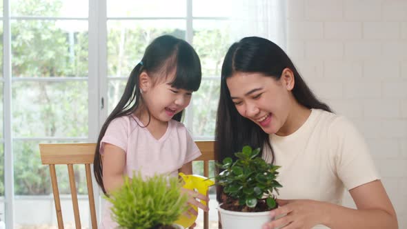 Asian family mom and daughter watering plant in gardening near window at house.