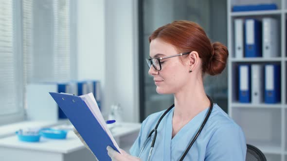 Female Physician in Safety Gloves Writes Notes in the Clipboard Happy Therapist in Glasses and Blue