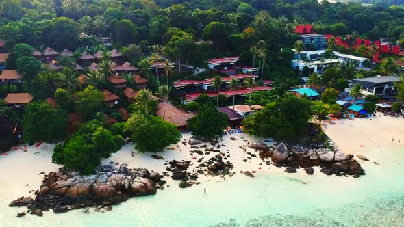 An aerial shot of  a resorts by the beach with few unrecognisable people walking along the shoreline