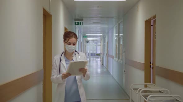 A Masked Doctor Walks Down the Corridor of the Hospital