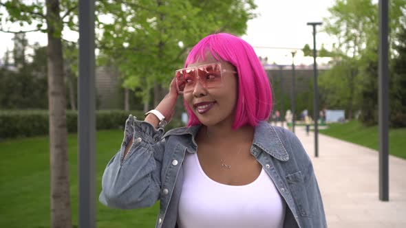 Young Stylish Black Woman with Pink Hair Walks in the Park on a Sunny Day