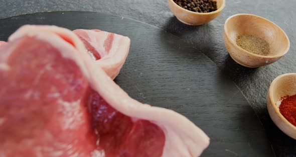 Sirloin chop and bowls of spices on concrete background