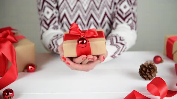 Female hands showing wrapped present in kraft paper box with red ribbon bow
