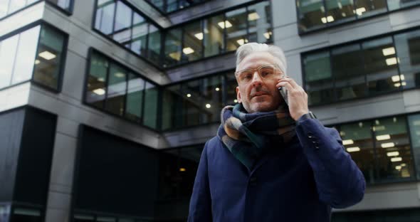 A Grayhaired Man Uses a Mobile Phone Standing in Business Center of the City