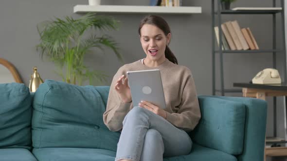 Woman Celebrating Success on Tablet on Sofa