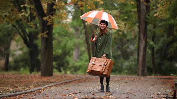 Redhead girl with suitcase and umbrella in autumn outdoor