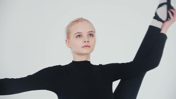 Young Woman Ballerina Raising Up Her Leg Against Her Body and Holding It