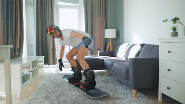 Fun Video. Man in Shorts and a T-shirt Depicts Snowboarding on a Carpet in a Cozy Room. Waiting for