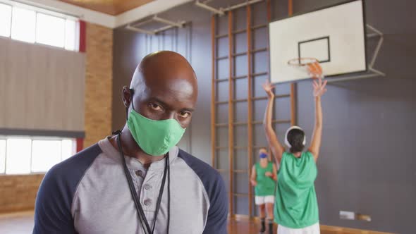 Portrait of african american male coach with diverse female basketball team in background