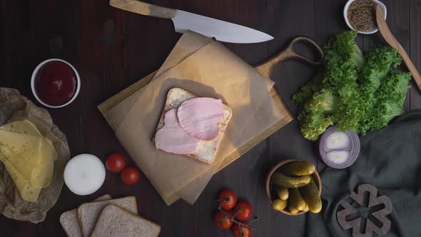 Flat Lay of the Sandwich with Sliced Ham and Vegetables on the Wooden Board in the Beam of Light