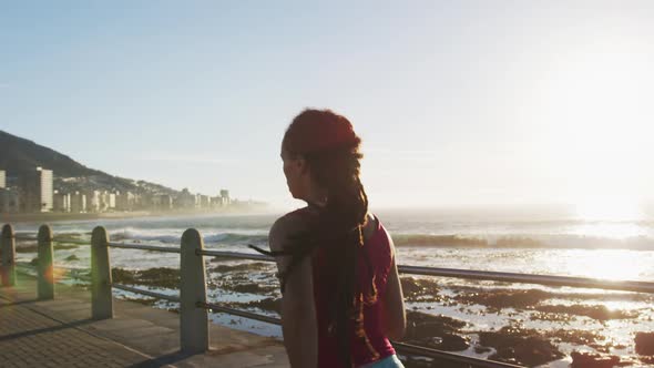 African american woman running on promenade by the sea at sundown