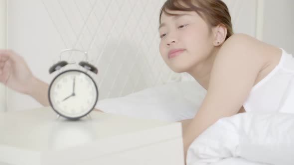Beautiful young asian woman panicked waking up in the morning looking clock and shock at home.