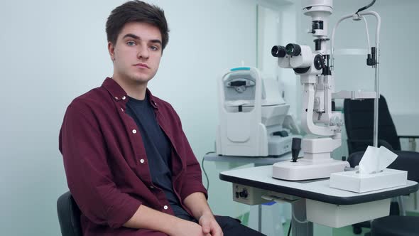 Medium Shot Portrait of Young Caucasian Man Sitting in Ophthalmologic Clinic at Retina Camera Posing